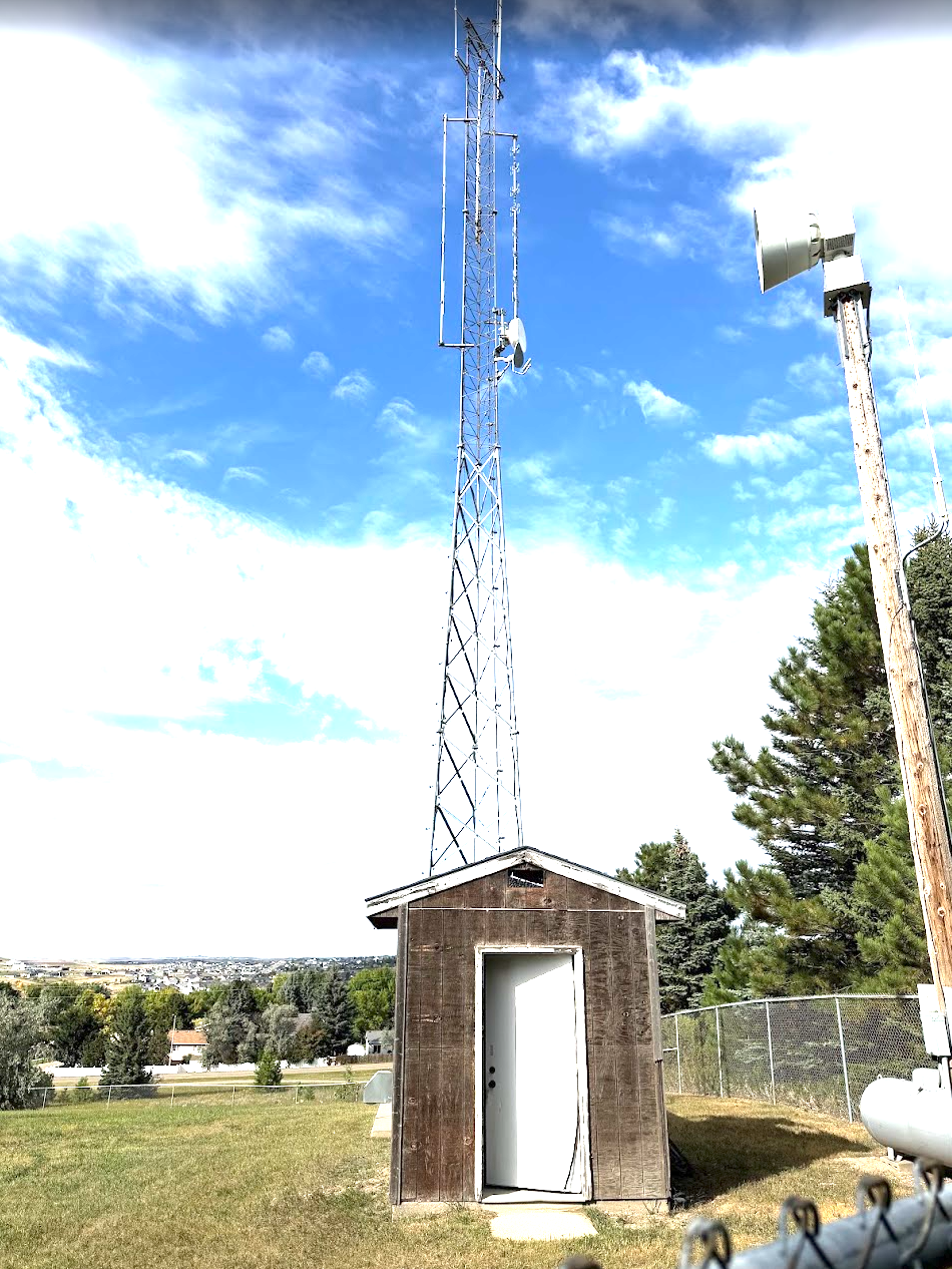 The Hillside ARC repeater shack and tower at the water tower site — door ajar, the building sitting vacant before it was ordered cleared